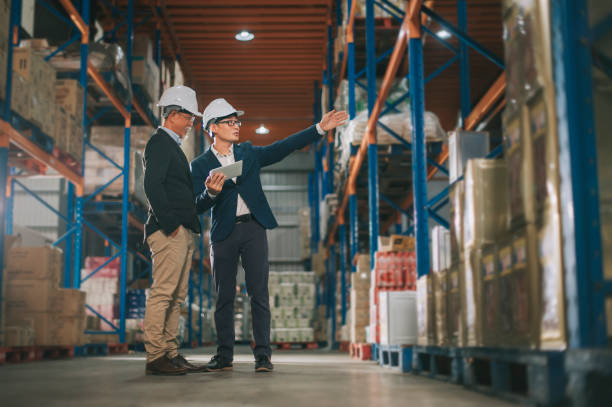 gestión china asiática teniendo discusión en el almacén con hardhat blanco usando tableta digital - logistical fotografías e imágenes de stock