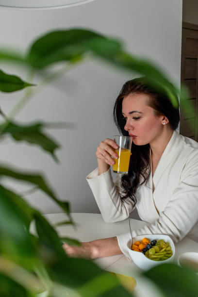 istock Young woman in comfortable white robe works on laptop while sitting at table the kitchen. Work at home for breakfast. 1316897179