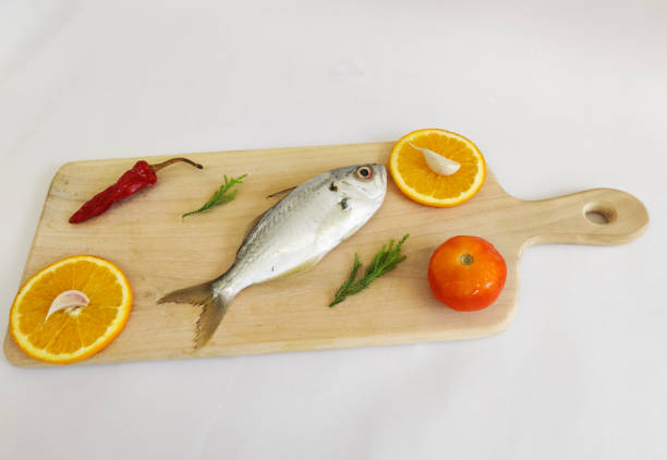 This photo shows a person wearing white gloves holding fresh fish between bars. The fish's scales and eyes are clearly visible. The fish sits on a shiny, white surface, which highlights the freshness of the fish. The photo provides a great visual for fresh fish and seafood. The ice crystals on the fish further highlight its freshness. The overall atmosphere of the photo highlights the clean, bright, and quality fish.