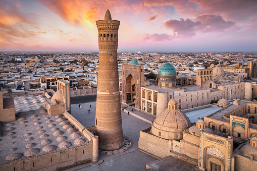 Colorful sunset twilight over the famous old town in the City of Bukhara with the iconic Kalyan Minaret and Mir-i-Arab Madressa. Aerial Drone Point of View. Itchan Kala, Bukhara, Khorezm Region, Uzbekistan, Central Asia.