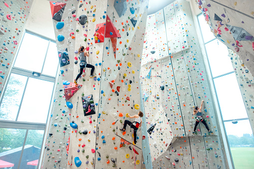 Wide angle perspective of 12, 22, and 23 year old Caucasian sportswomen ascending high vertical and inclined slabs in modern sport climbing facility.