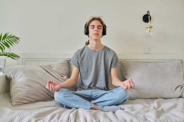 瞑想をリラックスベッドの上に蓮の位置に座っている男性ティーンエイジャー - lotus position audio ストックフォトと画像