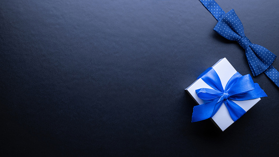Gift dad. Blue bowtie or tie, white box with bow ribbon on dark background. Happy loving family and Fathers Day concept