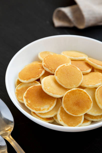 istock Homemade Mini Pancakes Cereal in a white bowl on a black background, side view. 1316911661