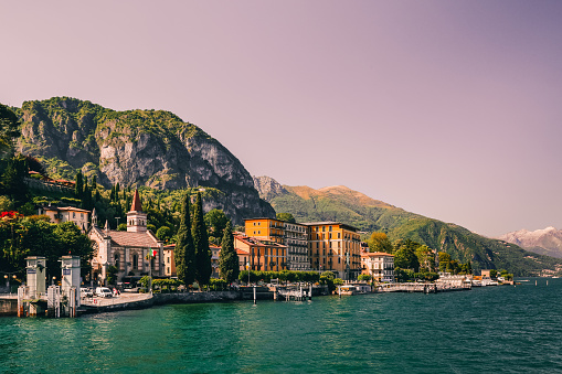 Blue peaceful Como lake (Lago di Como) in sunny evening, Cadenabbia, Northern Italy scene. Expensive tourist destination and holiday. Forest and hills, gorgeous harbour, old embankment with boat pier