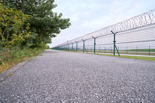 Asphalt path by the airport's barbed wire fence，Asphalt road outside the fence of the guard zone