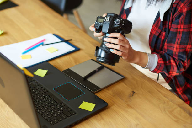 クリエイティブオフィスで働く写真家女性がカメラを持ち、机とレタッチ写真で - ポスプロスタジオ ストックフォトと画像