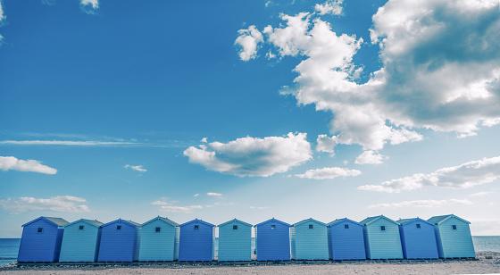 Bright blue beach huts on a sunny day with a clear sky and fluffy white clouds, UK Dorset Devon border.