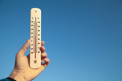 Hand holding thermometer on blue sky background.