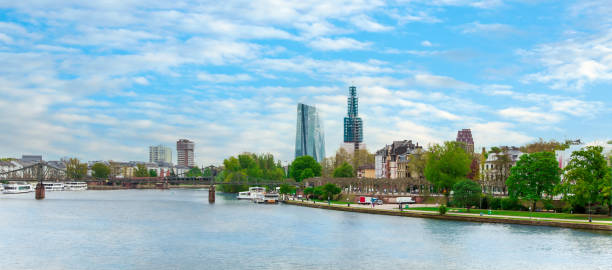 View of the river Main with skyscraper buildings and a church under construction. Skyline Frankfurt view from the Bridge - Untermainbrücke on blue clouds sky. High-rise buildings in Frankfurt - Main in Germany, Hesse panoramic riverbank architecture construction site stock pictures, royalty-free photos & images