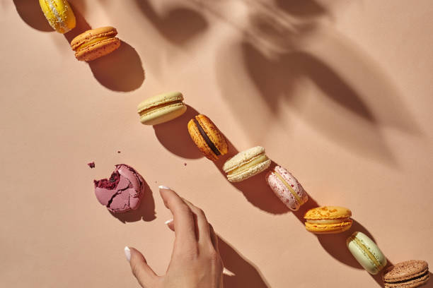 istock Female hand reaching for bitten macaron on beige background 1316925450