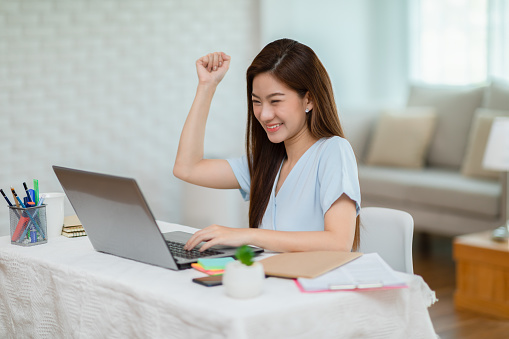 Entrepreneur of beautiful business asian young woman working online with laptop and celebrating at home with her work success cheerful and happiness,Small Business Startup concept