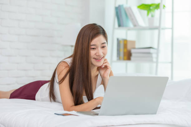 istock Beautiful Attractive Asian young woman lying on bed and using computer laptop for using social media and shopping online relax in cozy bedroom in holiday,Lifestyle in home Concept 1316926438
