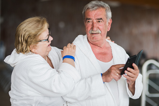 Senior man using smart phone on the pool and his wife hugging him and smiling