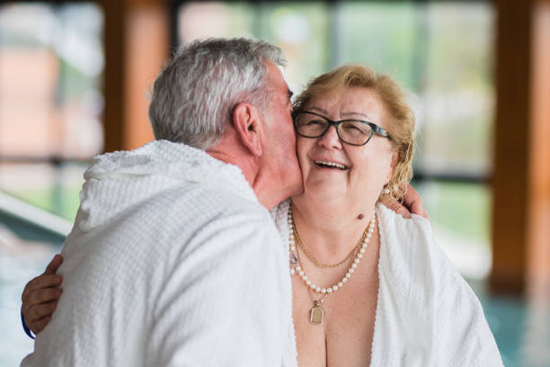 seniorin steht auf schwimmbad und lacht, wenn sie von ihrem mann geküsst wird - overweight smiling senior women 70s stock-fotos und bilder