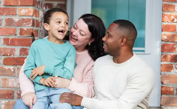 Photo of Interracial family with boy sitting on front stoop