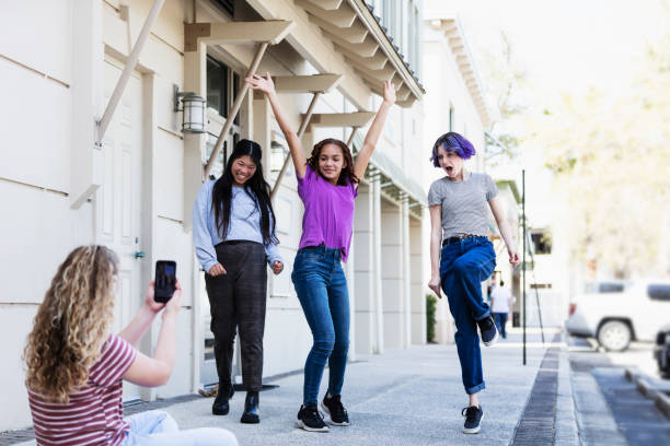 Tween girl filming friends with smart phone A multi-ethnic group of four tween girls, 12 and 13 years old, hanging out together on a sidewalk outside a building. One of the girls is filming or photographing her friends with her smart phone as they pose and dance. influencer photos stock pictures, royalty-free photos & images