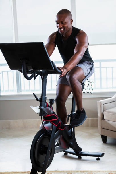 hombre afroamericano en bicicleta de ejercicios en casa - bicicleta estática fotografías e imágenes de stock