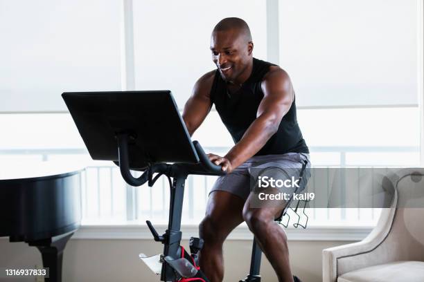 Africanamerican Man On Exercise Bike At Home Stock Photo - Download Image Now - Exercise Bike, Domestic Life, Home Interior