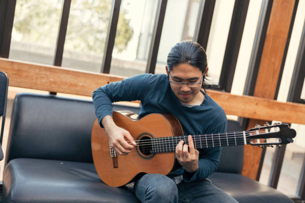 istock Young Asian man playing guitar in living room 1316943521