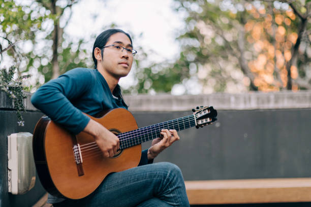 młody azjatycki tajski mężczyzna gra na gitarze w parku w mieście - 20s acoustic guitar adult art zdjęcia i obrazy z banku zdjęć