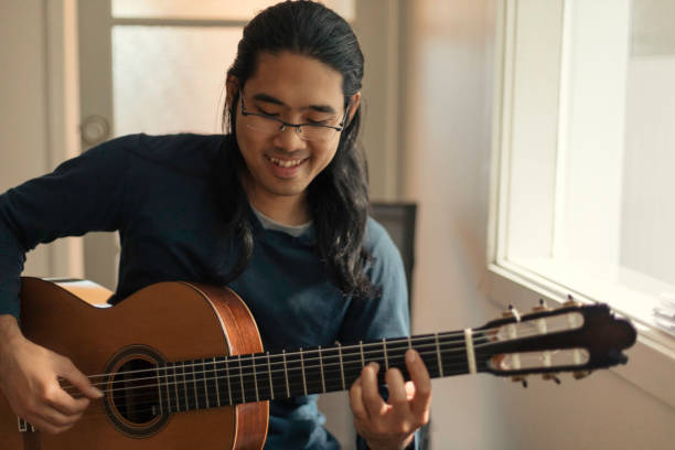 istock Young Thai Asian man playing guitar at home during lockdown 1316943637