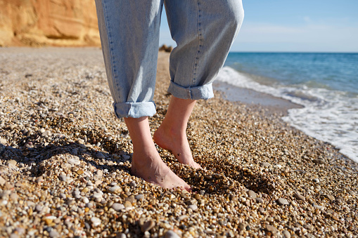 close-up photo. bare feet in tucked up jeans on the sand.