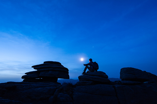 Silhouette of the outdoor hikers reading in the moonlight on the mountain