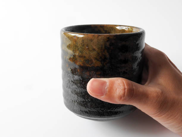 istock Pick up a dark brown pottery cup in one hand isolated on white background. 1316954465