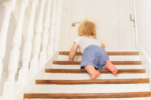 Cute little toddler boy climb on the stairs at home view from behind