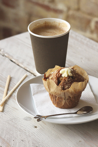 A takeaway cup with a hot drink and a muffin.