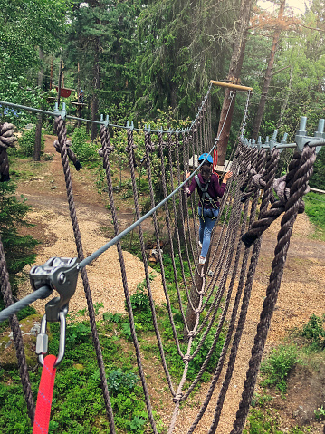 A girl crossing a rope bridge in a forest with safety equipment attached.