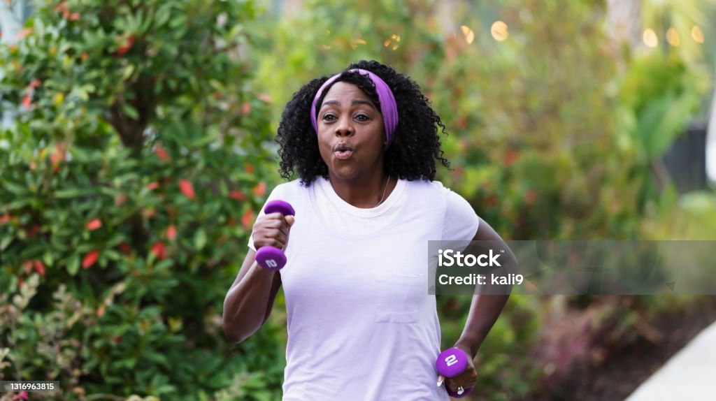 Senior African-American woman exercising outdoors A senior African-American woman in her 60s exercising outdoors. She is power walking or jogging, with dumbbells in her hands. Senior Adult Stock Photo