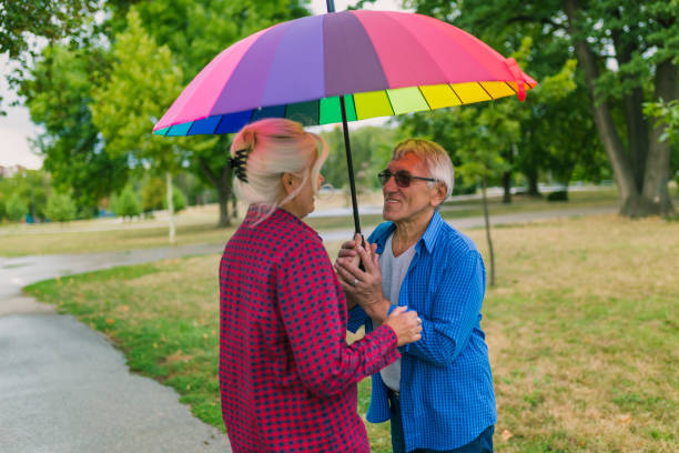 couples marchant dans le jour humide - umbrella senior adult couple autumn photos et images de collection