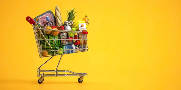 Photo of Shopping cart full of food on yellow background. Grocery and food store concept.