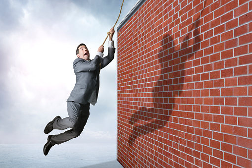 A businessman swings from a rope as he realizes he is about to swing into a wall.