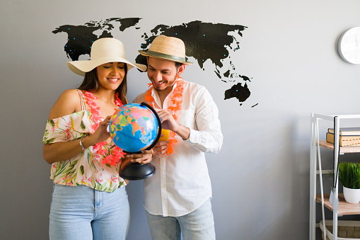 We are traveling here. Good-looking tourists looking at a world globe and choosing their next tropical destination at the travel office
