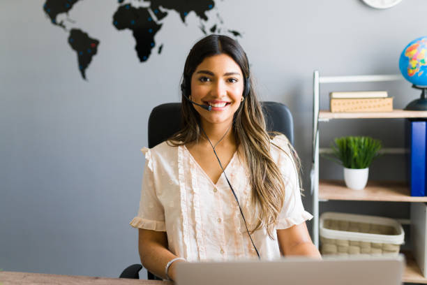 Yes, how can I help you with your flight? Making a sale. Happy young woman with a headset talking with a potential customer about booking a tourist trip abroad at the travel agency travel agency stock pictures, royalty-free photos & images