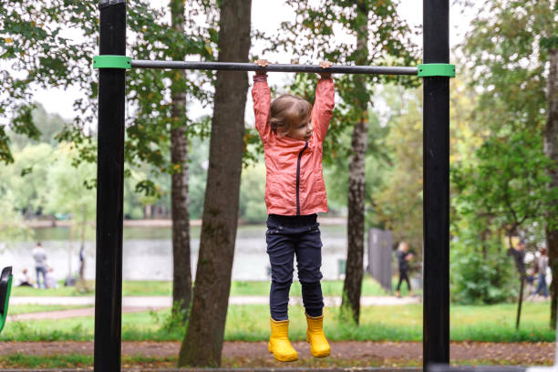 kid hangs on a horizontal bar in an autumn park a little girl hangs on a horizontal bar in an autumn park horizontal bar stock pictures, royalty-free photos & images