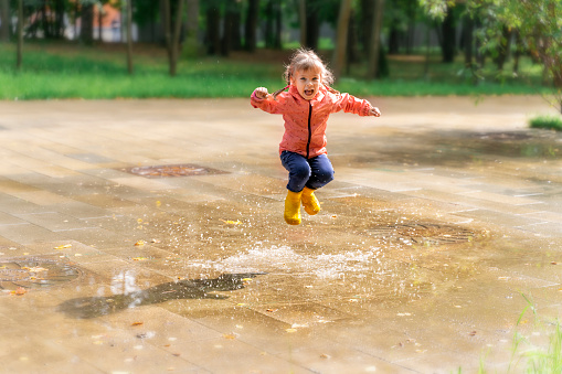 happy child girl in rainboots has the delight of jumping through puddles