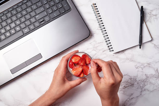 Top view of woman hands writing in blank notebook and glass of healthy yogurt with fresh sliced strawberry on white table, copy space. Healthy food concept. Flat lay stock photo