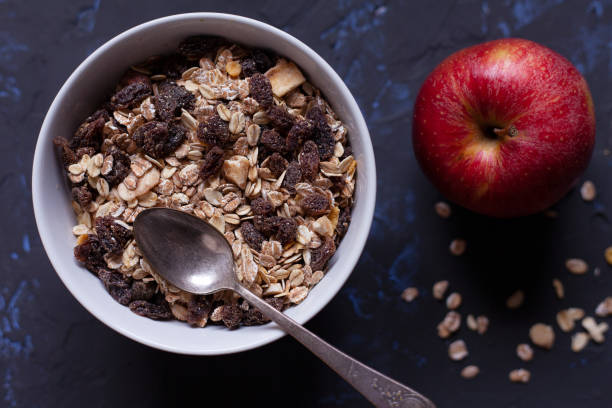 istock Bowl with muesli with a spoon, and an apple on a black background viewed from above. 1316981848