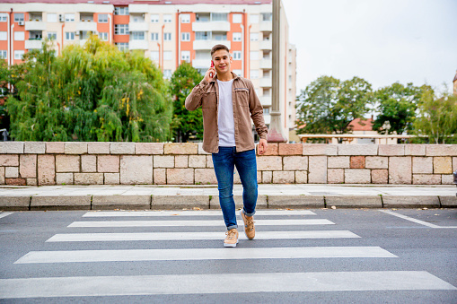 Young cheerful man crossing the street and talking on the mobile phone