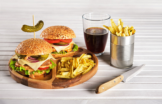 Homemade burgers with potato chips and cola in a glass on a light wooden background. Fast food. Horizontal orientation, no people, copy space.