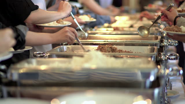 A group of people lined up to scoop up the food in the buffet line. Focusing on the hands of everyone who was scooping the food.