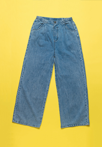 Stylish wide denim women's pants on a yellow background. Denim pants.