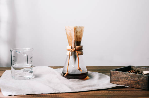 Manual glass coffee pot with filter and coffee on a gray cloth on a wooden table. Front view Manual glass coffee pot with filter and coffee on a gray cloth on a wooden table with coffee bean container and glass measuring jug on the sides. Front view coffee filter stock pictures, royalty-free photos & images