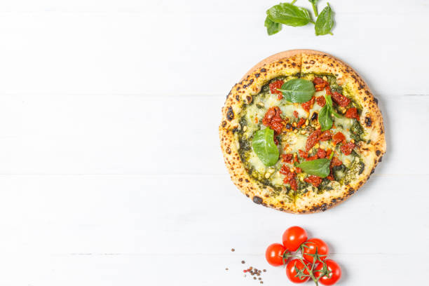 Pizza marinara bianca with pesto sauce, mozzarella, dried tomatoes, spinach and pine nuts. Close-up on a light wooden background, overhead with copy space stock photo