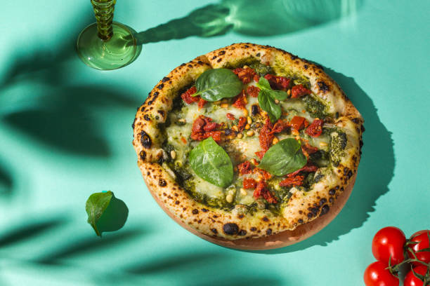 Pizza Margherita bianca with spinach and pesto on a bright green background with a glass of wine. Beautiful shadows, hard light stock photo