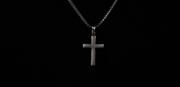 Praying with a rosary. hand of Catholic man with rosary on black background. Hands holding a silver rosary or cross pendant of Jesus Christ. Crucifix and hand on black background. Praying to God concept.